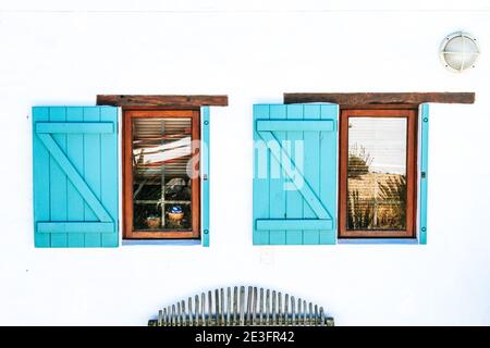 Weiße Hausfassade mit zwei Holzfenstern und türkisfarbenen Fensterläden Stockfoto