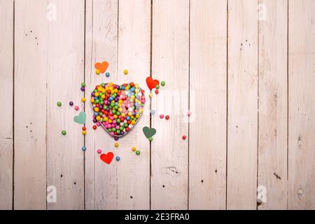 Ein herzförmiger Kasten, gefüllt mit regenbogenartigen Kugeln auf einem Holztisch. Farbige Herzen rund um Sie daran zu erinnern, dass Liebe hat viele Schattierungen. Stockfoto