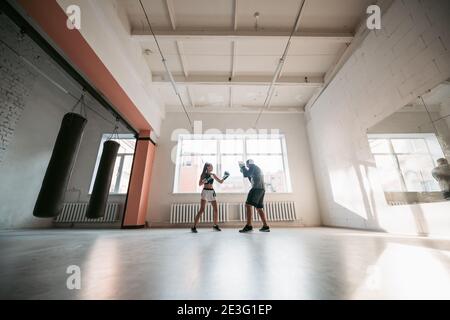 Eine junge Sportlerin in guter körperlicher Verfassung führt Kickboxen durch Training unter der Aufsicht eines erfahrenen Trainers Stockfoto