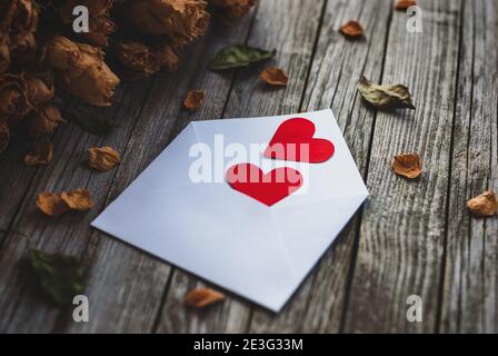 Zwei Herzen im Umschlag, Blütenblätter von trockenen Rosen auf Holztisch Stockfoto