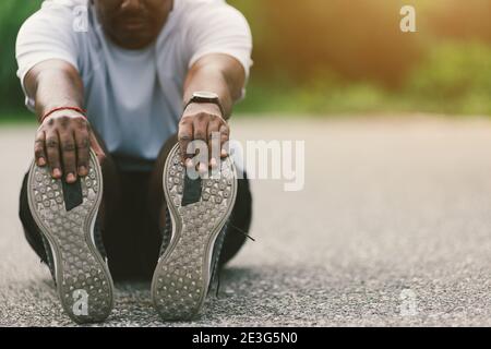 Nahaufnahme Asian junge Athlet Sport Läufer schwarz Mann tragen beobachten er sitzen ziehen Zehe Füße Stretching Beine und Knie vor dem Laufen im Freien Street heilen Stockfoto