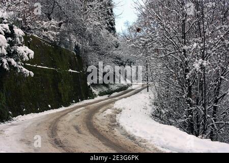 Holprige und schlecht gepflasterte Straße Weg auf Berg Winterschnee Weißer Feldweg im Wald in der toskana Stockfoto