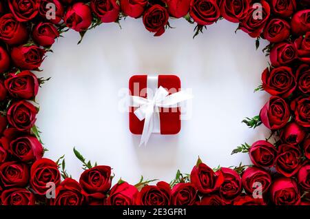 Rote Geschenkbox auf weißem Hintergrund mit Rosenrahmen für Jubiläum und Valentinstag-Konzept. Stockfoto