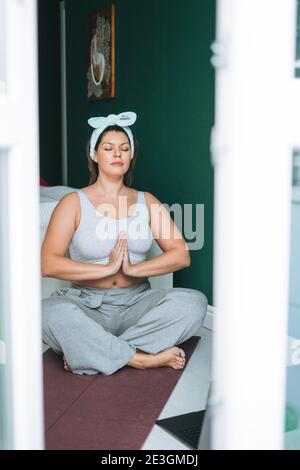 Schöne Brünette junge Frau plus Größe Körper positiv in komfortabel Sportbekleidung Yoga zu Hause online üben Stockfoto