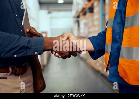 Mittelansicht von zwei männlichen Arbeitern, die sich in der Fabrik die Hände schüttelten Stockfoto