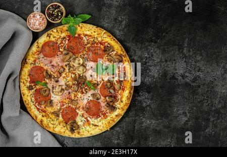 Frische italienische Pizza mit Pilzen, Schinken, Tomaten, Käse auf schwarzem Hintergrund. Stockfoto