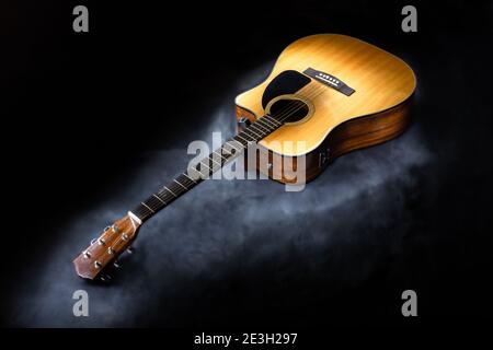 Akustische 6-saitige Gitarre in klassischer gelber Farbe auf isoliertem Schwarz Hintergrund umgeben von Nebel Stockfoto