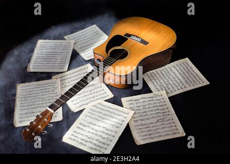 Klassische gelbe Farbe akustische sechs-Saiten-Gitarre und Noten Buchstaben Mit Noten auf isoliertem schwarzem Hintergrund umgeben von Nebel Stockfoto