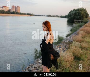 Rothaarige Frau in einem schwarzen Kleid in der Nähe des Flusses in Natur Stockfoto