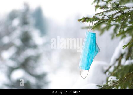 Gebrauchte chirurgische oder medizinische Schutzmaske aufgegeben oder entsorgt als Der Abfall oder der Müll auf dem Ast des Baumes mit Natur im Hintergrund Stockfoto