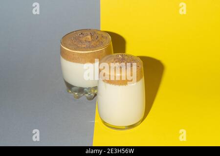 Zwei Gläser Dalgon-Kaffee mit üppigem Schaum auf grau-gelbem Hintergrund, trendigen koreanischen Getränk. Stockfoto