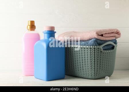 Korb mit Handtüchern und Flaschen mit Wäscheflüssigkeit auf weiß Holztisch Stockfoto