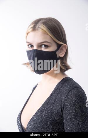 Ein 19-jähriges ruhiges Mädchen mit Bob-Frisur und gebleicht Stränge in einem grauen Top mit laurix und grau breit Hose mit schwarzer medizinischer Maske auf ihr Stockfoto