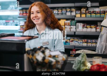 Frau, die an der Kasse eines Supermarkts arbeitet. Weibliche Kassiererin, die an der Kasse des Lebensmittelladens arbeitet. Stockfoto