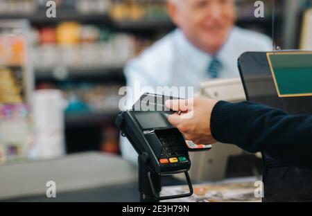 Nahaufnahme eines Kunden zahlt für den Einkauf an einer Supermarktkasse. Kunde, der in einem Geschäft mit einer Kreditkarte bezahlt. Stockfoto