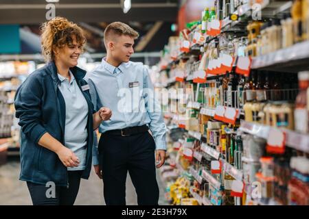 Weibliche Führungskraft hilft neuen männlichen Auszubildenden im Lebensmittelgeschäft. Mann im Urlaub Job bekommen Hilfe vom Manager im Supermarkt. Stockfoto