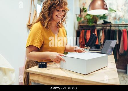 Frau bereitet ein Paket für die Lieferung für eine Online-Bestellung vor. Frau läuft Online-Shop aus ihrer Mode-Boutique. Stockfoto