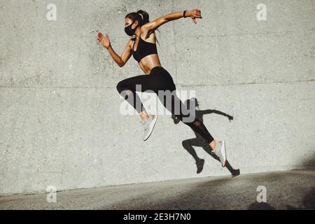 Fitness Frau trägt Gesichtsmaske läuft im Freien. Frau Athlet Training im Freien am Morgen. Stockfoto