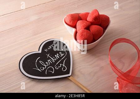 Herzförmiges Poster mit glücklicher Valentinstags-Botschaft und Gelee-Süßigkeiten und Erdbeerzucker in herzförmigem Behälter. Erhöhte Ansicht. Stockfoto