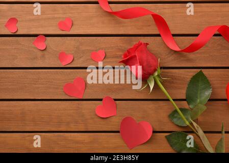 Romantischer Hintergrund mit roter Rose und roten Ausschnitten mit Herzform auf Holzlattentisch und Bogen. Draufsicht. Stockfoto