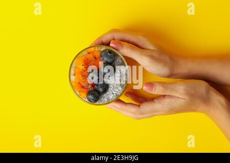 Weibliche Hände halten Glas Chia Pudding auf gelbem Hintergrund Stockfoto