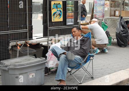 Mann schläft in der Straße in New York USA Sesselbehälter Plastikschilder Arbeiter Arbeitsweg Straßenverkäufer Verkaufsregale Huttasche Plastikmantel Stockfoto