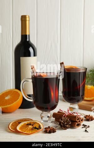 Rotweinflasche und Tassen mit heißem Glühwein auf Holzplanken, eine Gruppe Glühweintrinker mit Wintergewürzen für einen festlichen Abend Stockfoto