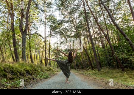 Weibliche Teenager-Tänzerin posiert im grünen Wald in grünem, langem Kleid Stockfoto