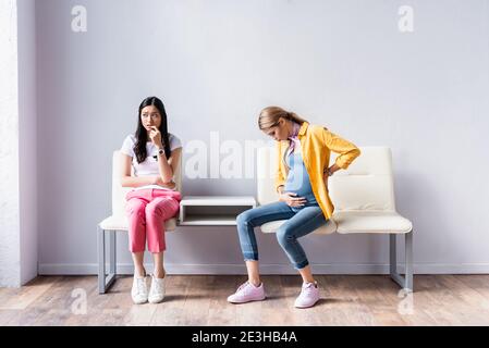 Schwangere Frau sitzt in der Nähe besorgt asiatische Frau in der Schlange Stockfoto