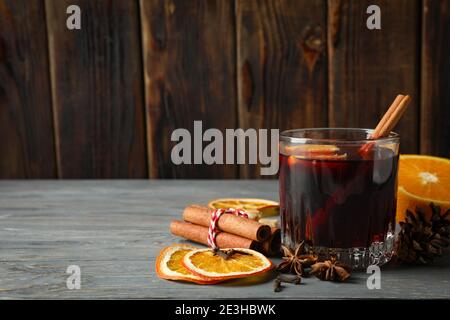 Heißer Glühwein in einem Glas mit Gewürzen auf einem grauen Holztisch, ein wärmender Winterglühwein mit Zimt und Zitrusfrüchten für Weihnachten Stockfoto
