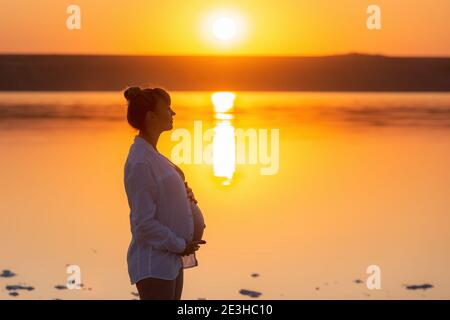 Schwangere Frau Seitenprofil Silhouette. Frau berührt ihren Bauch. Wunderschöner Sonnenuntergang Stockfoto