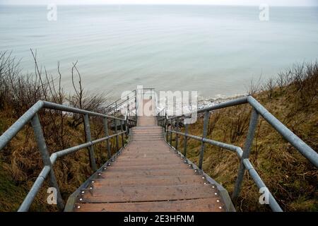 Nienhagen, Deutschland. Januar 2021. Eine Treppe führt zum Strand an der Ostseeküste. Das russische Lay-Schiff "Fortuna" ist in der Ostsee vor dem Hafen von Rostock verankert, kaum sichtbar im Nebel und Schneeregen. Das Spezialschiff soll für Bauarbeiten an der deutsch-russischen Nord Stream 2 Ostsee-Gaspipeline eingesetzt werden. Die USA wollen erstmals Sanktionen gegen die Gaspipeline verhängen. Die Strafmaßnahmen betreffen das russische Laienschiff "Fortuna", das am Bau der Pipeline beteiligt ist. Quelle: Jens Büttner/dpa-Zentralbild/dpa/Alamy Live News Stockfoto