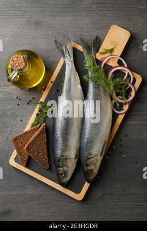 Tafel mit Heringfisch und Gewürzen und Öl auf dunklem Holzhintergrund Stockfoto