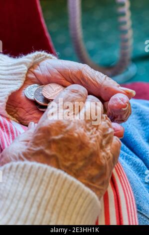 Eine ältere Dame zählt sorgfältig Geld mit Münzen in ihren Händen. Stockfoto