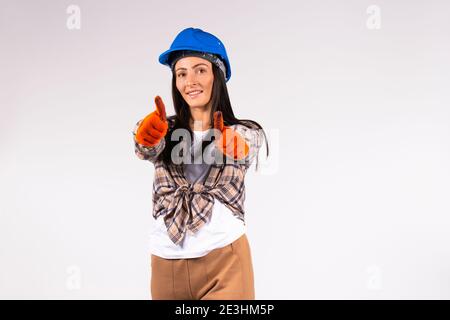 Lächelnde Mechanikerin in Helm und Handschuhen zeigt der Kamera die Klasse. Weißer Hintergrund mit leerem Raum. Stockfoto