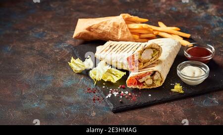 Traditionelle Shawarma, Döner Kebab mit Huhn und Gemüse und Pommes mit Soßen auf Schiefer. Fast Food. Östliches Essen. Stockfoto