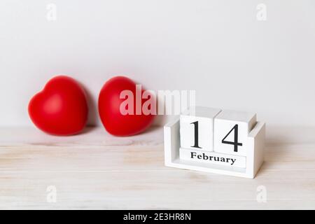 Holzkalender zeigt Februar 14 und rote Herzen dahinter. Valentinstag. Speicherplatz kopieren. Selektiver Fokus Stockfoto