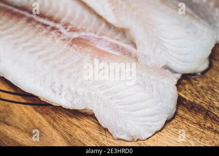 Nahaufnahme von rohem, ungekochten weißen Fischfilet. Pangasius oder Kabeljaufilet isoliert auf Holzgrund. Stockfoto