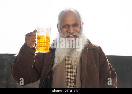 EIN FRÖHLICHER ALTER MANN HÄLT GLÜCKLICH EIN GLAS BIER Stockfoto