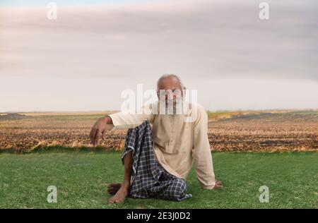 EIN LÄNDLICHER ALTER MANN, DER GLÜCKLICH AUF DEM ACKERLAND SITZT Stockfoto