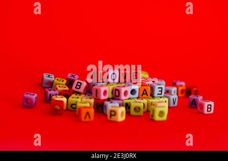 Bunte Holzwürfelperlen mit Buchstaben auf rotem festlichem Hintergrund, Wort "Liebe". Valentinstag. 14 Februar. Flach liegend, Draufsicht. Stockfoto