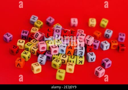 Bunte Holzwürfelperlen mit Buchstaben auf rotem festlichem Hintergrund, Wort "Liebe". Valentinstag. 14 Februar. Flach liegend, Draufsicht. Stockfoto