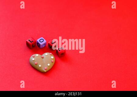 Festlicher roter Hintergrund. Herzförmige Kekse. Bunte Holzwürfelperlen mit dem Wort "Liebe". Valentinstag. 14 Februar. Geschenkideen. Flache Lay, Stockfoto