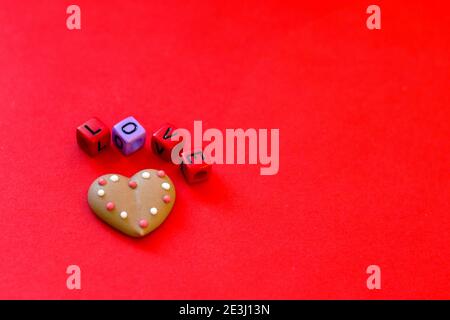 Festlicher roter Hintergrund. Herzförmige Kekse. Bunte Holzwürfelperlen mit dem Wort "Liebe". Valentinstag. 14 Februar. Geschenkideen. Flache Lay, Stockfoto