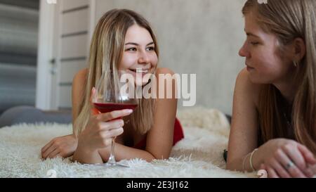 Zwei Freunde liegen auf der Couch und plaudern. Schöne Blondine hält ein Glas Rotwein in der Hand Stockfoto