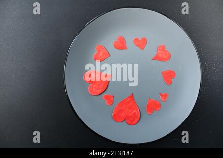 Rote Herzen auf einer grauen Platte auf schwarzem Hintergrund mit einem Copyspace Platz für Text. Stockfoto