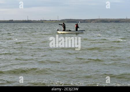 Zwei Männer fliegen Fischen von einem kleinen Boot auf Anglian Waters Grapham Wasserreservoir im Dezember. Stockfoto