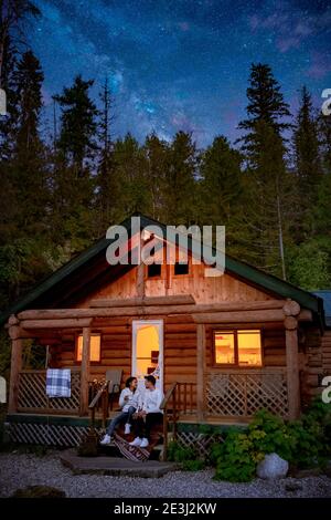 Kanada British Columbia Hütte im Wald in der Nacht, Paar trinkt vor der Holzhütte, EINE abgelegene Hütte Lodge vor der Milchstraße. Kanada Wald Wald Wald Hütte Stockfoto