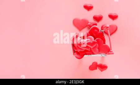 Trolley Warenkorb mit vielen Herzen auf rosa Hintergrund gefüllt. Konzept des Einkaufens für Valentinstag. Platz für Text kopieren. Stockfoto