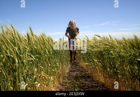 Laufen im Weizen Junges Mädchen, das im Spätsommer durch Weizenfeld läuft. Stockfoto